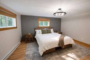 A bedroom with a large bed, a nightstand, a bedside table, a window, and a ceiling light fixture. - Moss Lake Lookout: PET Friendly (Lac du Flambeau)