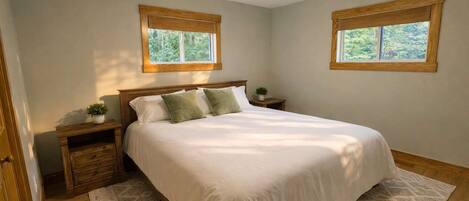 A bedroom with a bed, wooden headboard, two nightstands, a ceiling fan, and two windows with wooden frames.