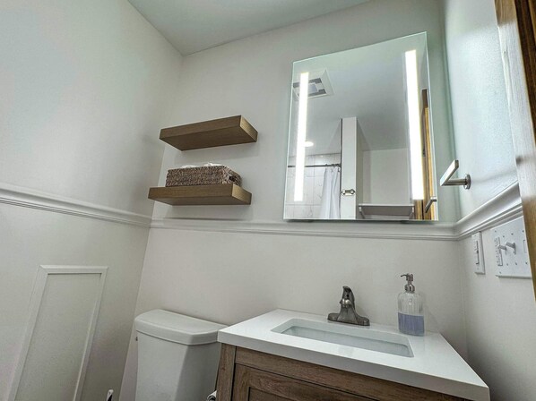 Une salle de bain avec un lavabo blanc, un miroir, des toilettes et des étagères en bois.