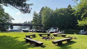 Zona verde con mesas de picnic y barcos amarrados cerca de un puente sobre el agua.