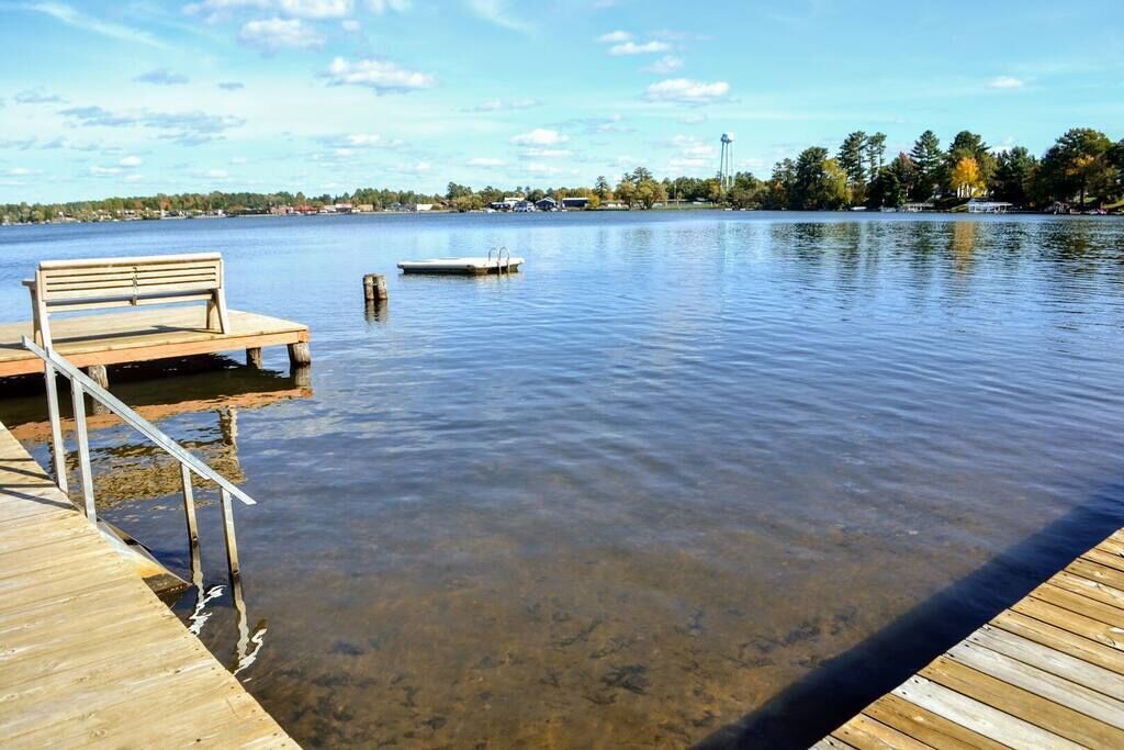 Un muelle de madera se extiende sobre un lago tranquilo con un banco y un bote pequeño.
