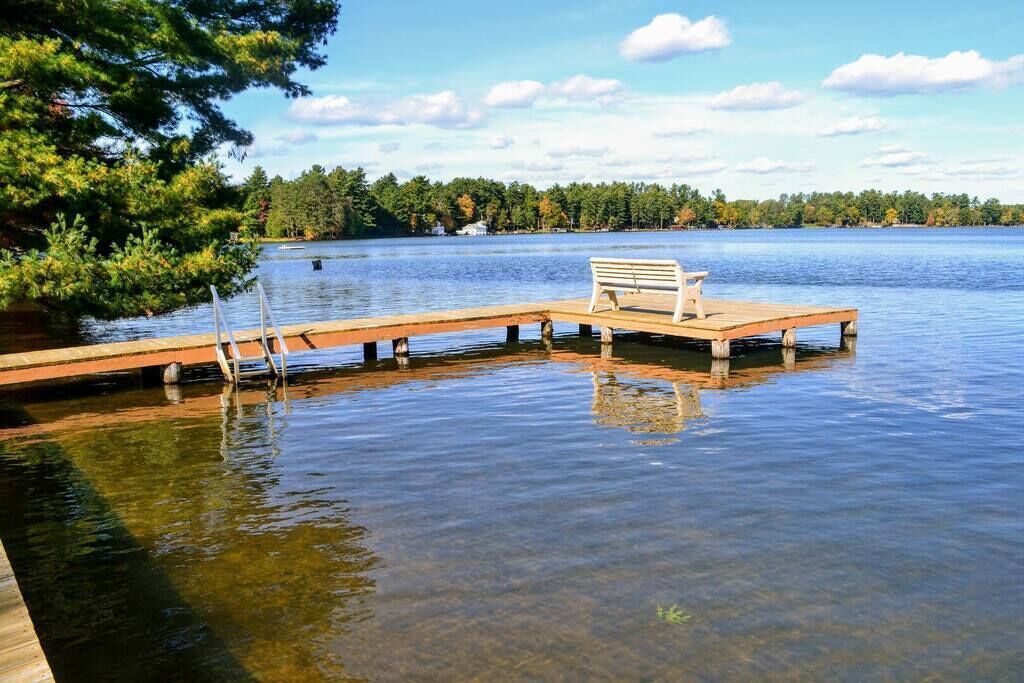 A wooden dock extending into a calm lake with a bench at the end.