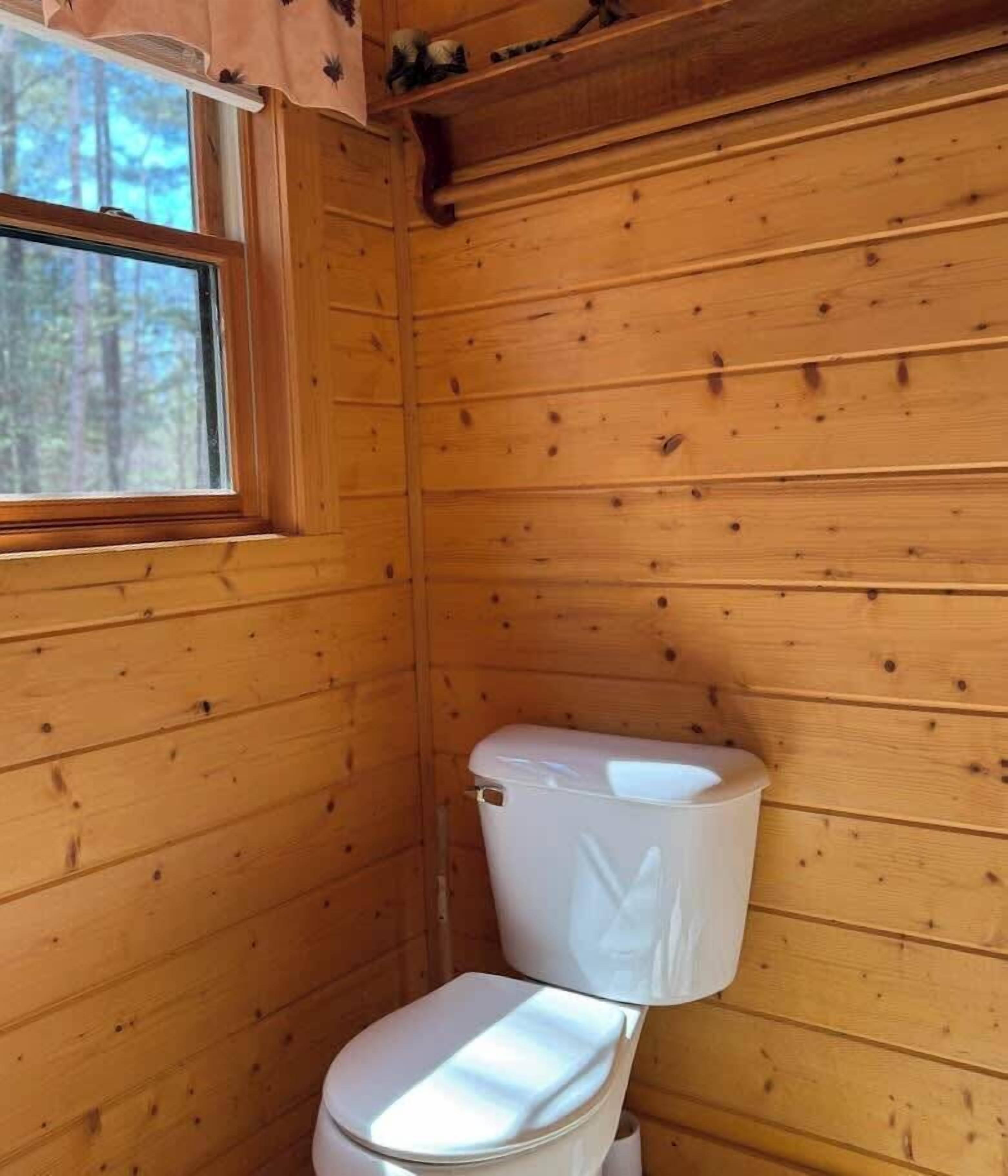 A wooden cabin bathroom with a toilet and a window.