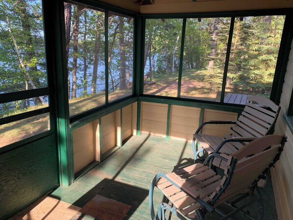 Eine überdachte Veranda mit Holzbänken und Blick auf Wald und See.