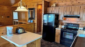 Une cuisine rustique aménagée dans une cabane en bois, comprenant un réfrigérateur, une cuisinière et un coin bar avec des tabourets.
