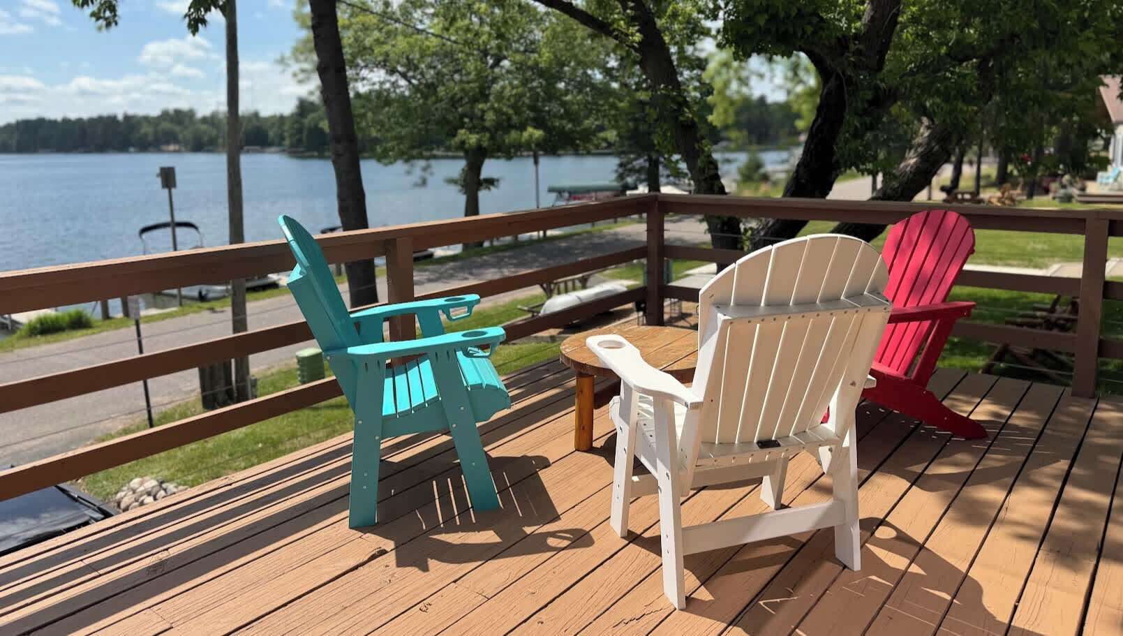 Une terrasse en bois avec deux fauteuils Adirondack et une petite table, donnant sur un lac.