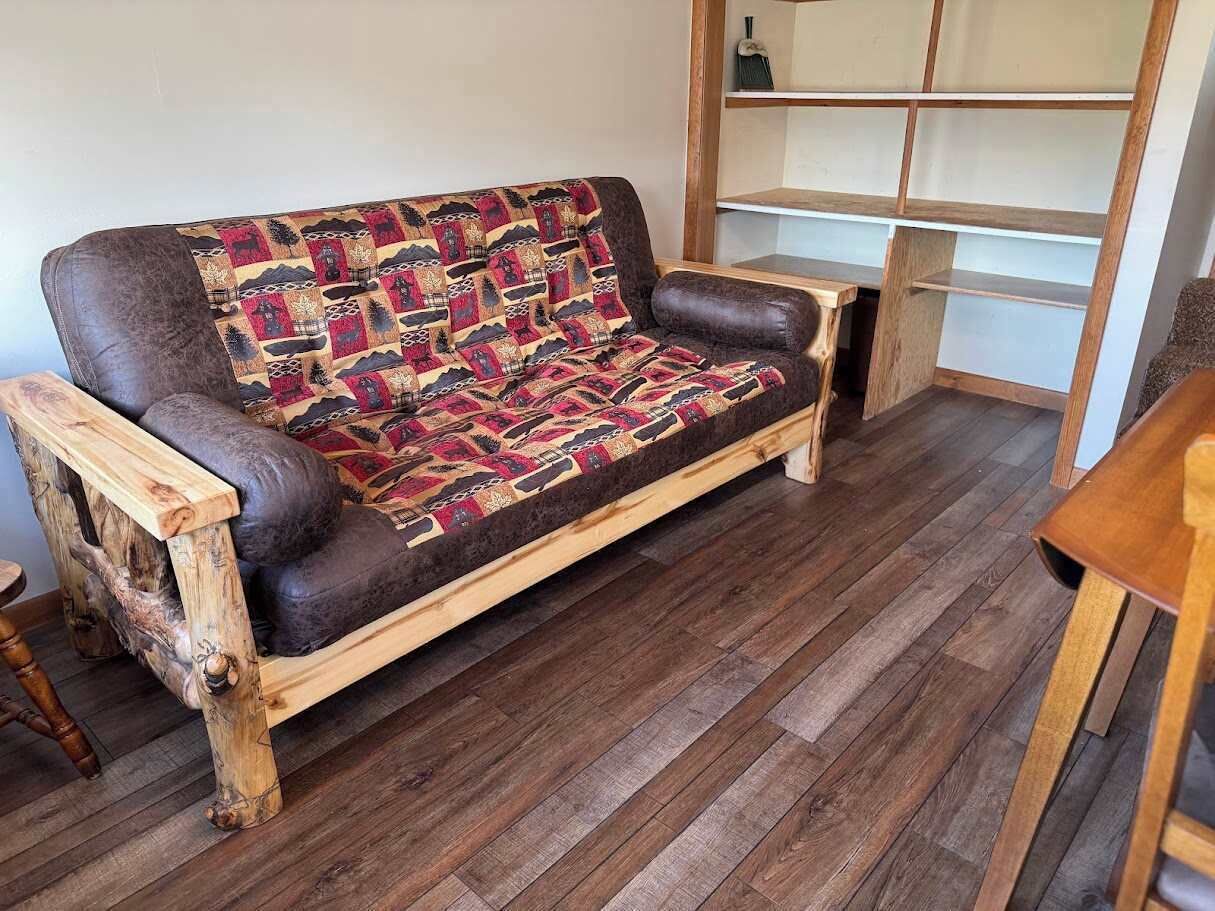 Un sofá de madera con un cojín estampado en una habitación con suelo de madera y una estantería.