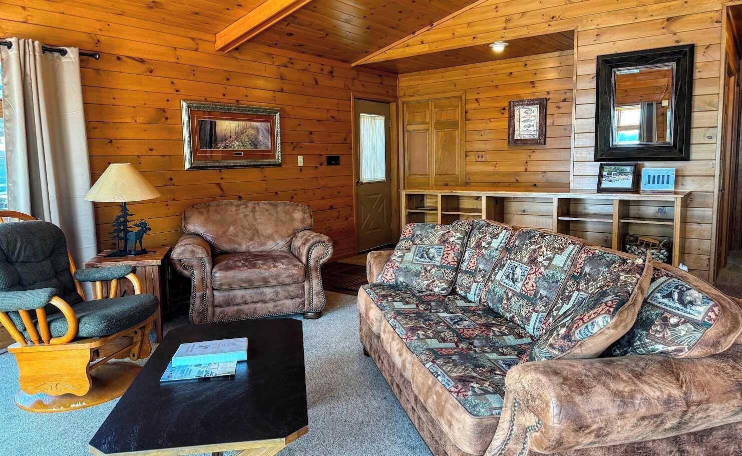 Un interior de cabaña acogedor con un sillón de cuero, un sofá estampado y una mesa de centro de madera.