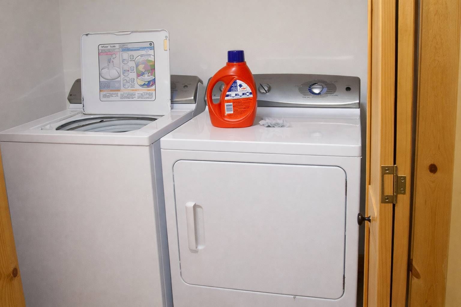 A laundry area with a washing machine and dryer, a detergent bottle, and a door with a latch.
