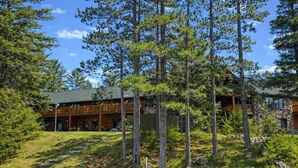 Een lodge met een houten terras, een stenen gebouw en een natuurlijke omgeving met bomen en water.