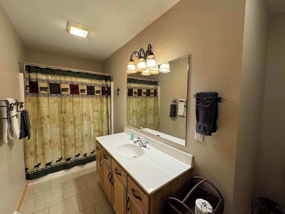 A bathroom with a wooden vanity, a sink, a mirror, and a shower curtain with animal patterns.