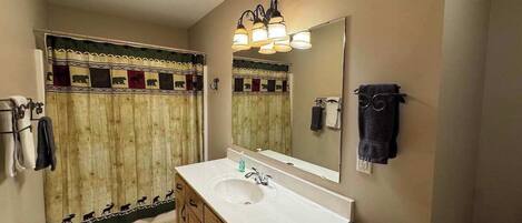 A bathroom with a wooden vanity, a sink, a mirror, and a shower curtain with animal patterns.