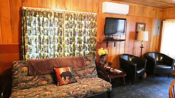 Una sala de estar acogedora con un sofá estampado, un televisor de pantalla plana y dos sillones de cuero.