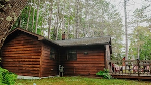 A wooden cabin with a porch, surrounded by a forest. - Old Stoney's Walleye- Pet Friendly (Woodruff)