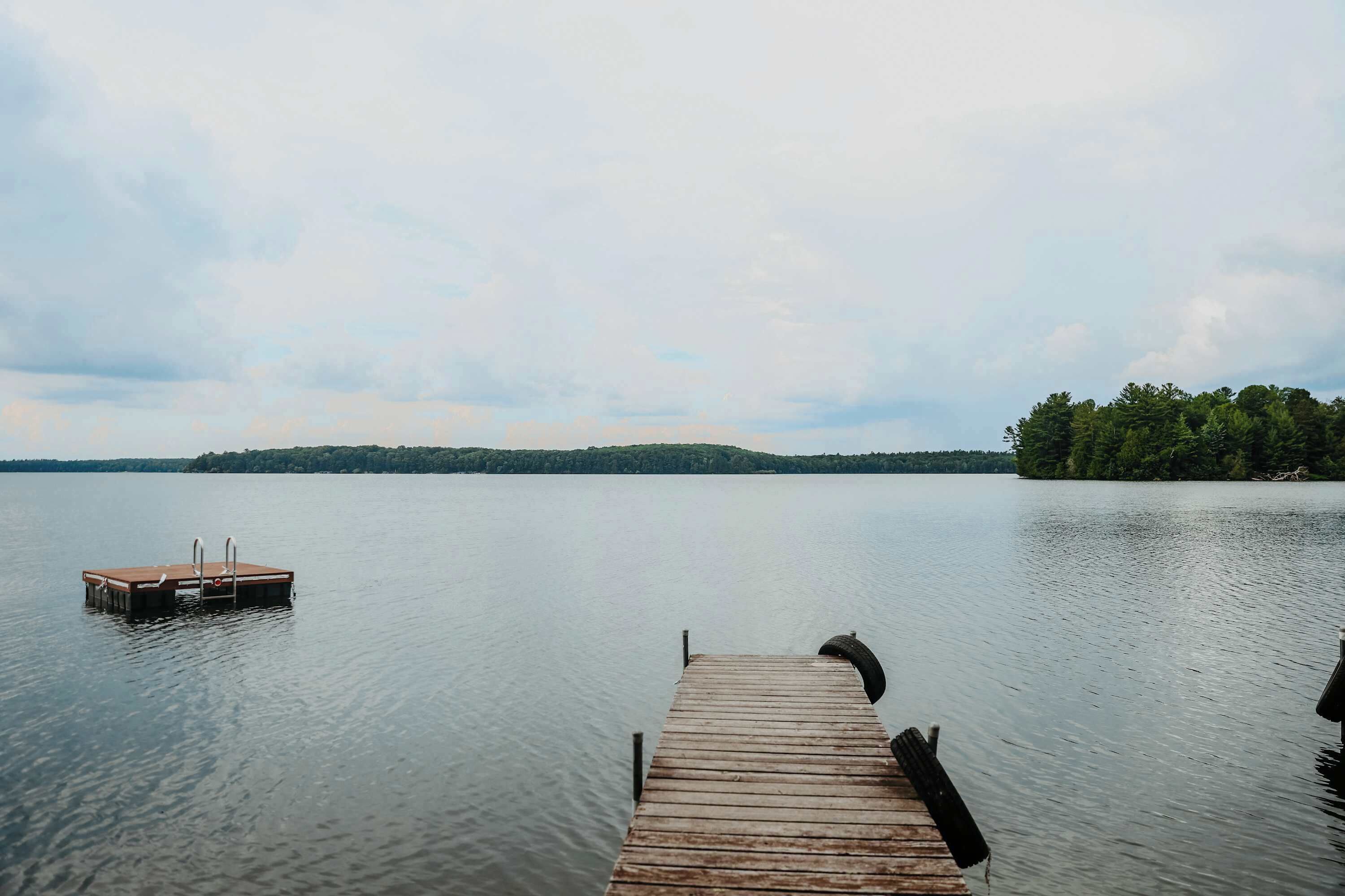 A wooden dock extending into calm water with a distant shoreline and trees.