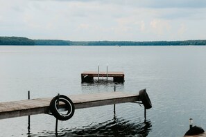 Eine Holzstege ragt in ruhiges Wasser hinein, an dem ein Reifen hängt.