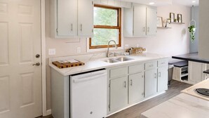 Una cocina moderna con armarios blancos, lavavajillas integrado y una ventana con vistas a zonas verdes.
