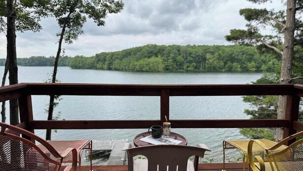 A wooden deck with two chairs and a small table, overlooking a lake with a forested shoreline. - Decompression Zone: Direct Access TO Snowmobile Trails (Woodruff)