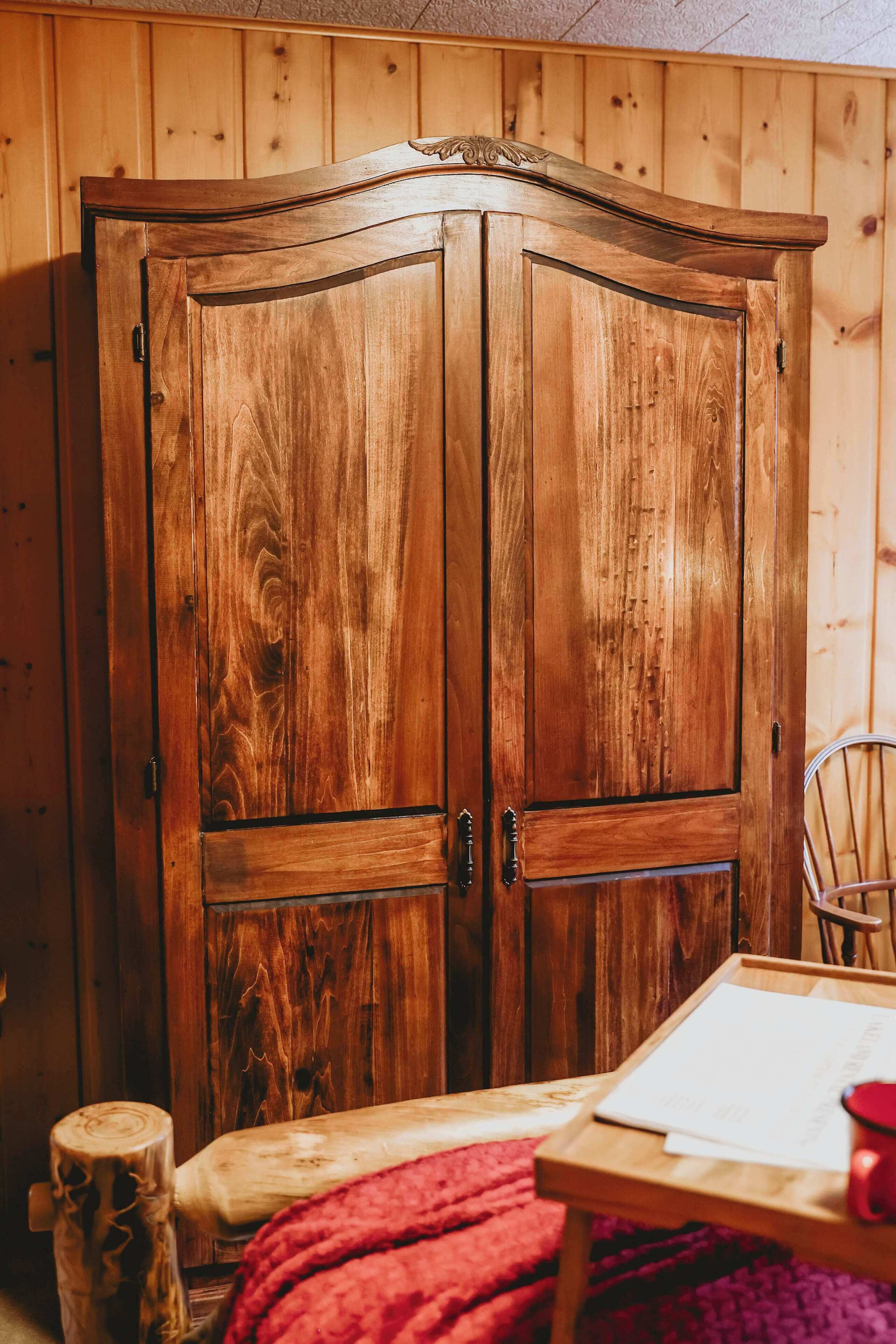 Un armario de madera con dos puertas, una mesita con una manta roja y una silla.