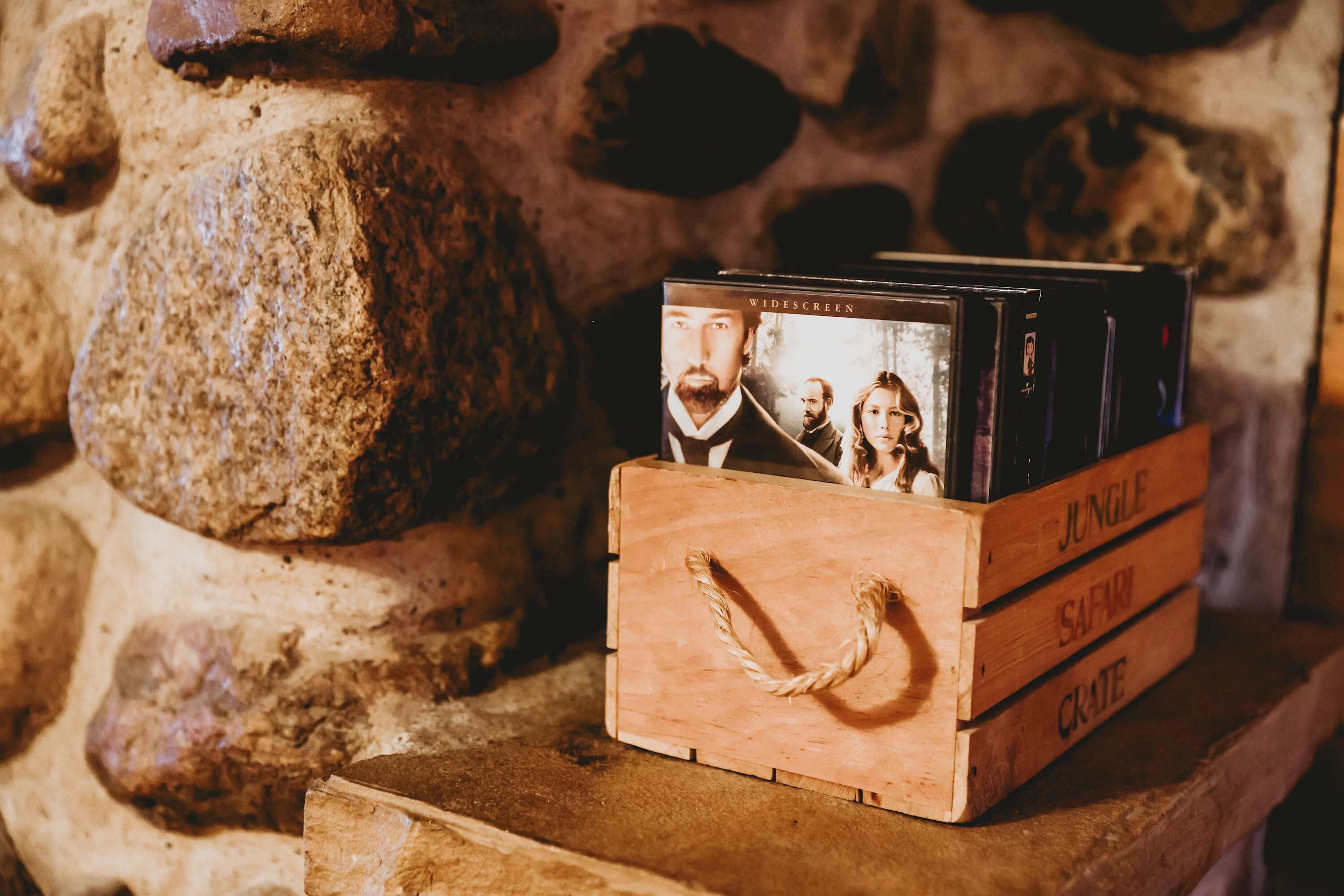 Una caja de madera con DVDs etiquetados 'Jungle', 'Safari' y 'Crate' sobre un fondo de pared de piedra.