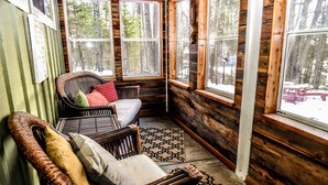 A cozy cabin interior with a wicker chair, a small bed, and large windows offering a view of the forest. - Decompression Zone: Direct Access TO Snowmobile Trails (Woodruff)