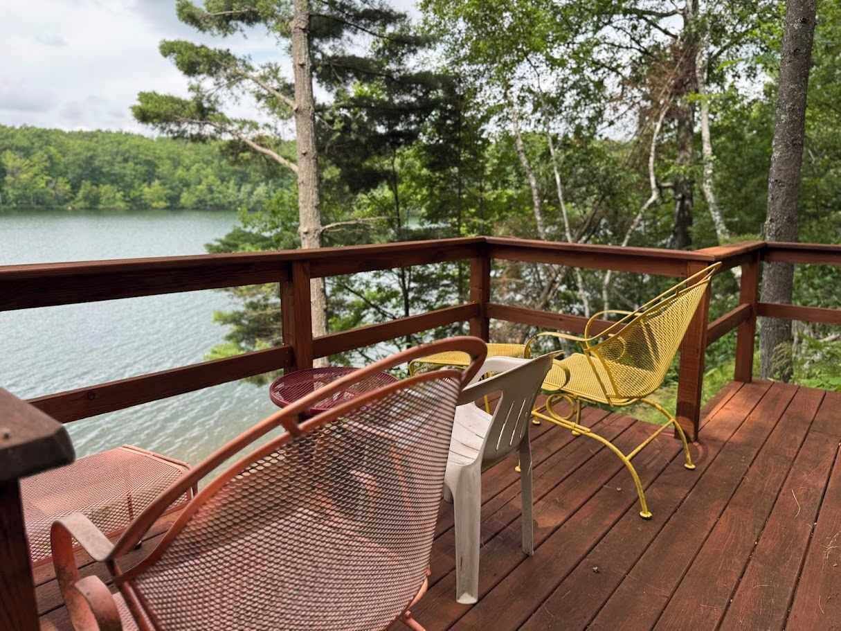 Une terrasse en bois avec des chaises en métal donnant sur un lac.