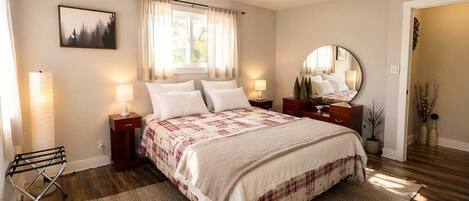 A bedroom with a bed, bedside lamps, a ceiling fan, a window with curtains, a bedside table, a mirror, and a rug.