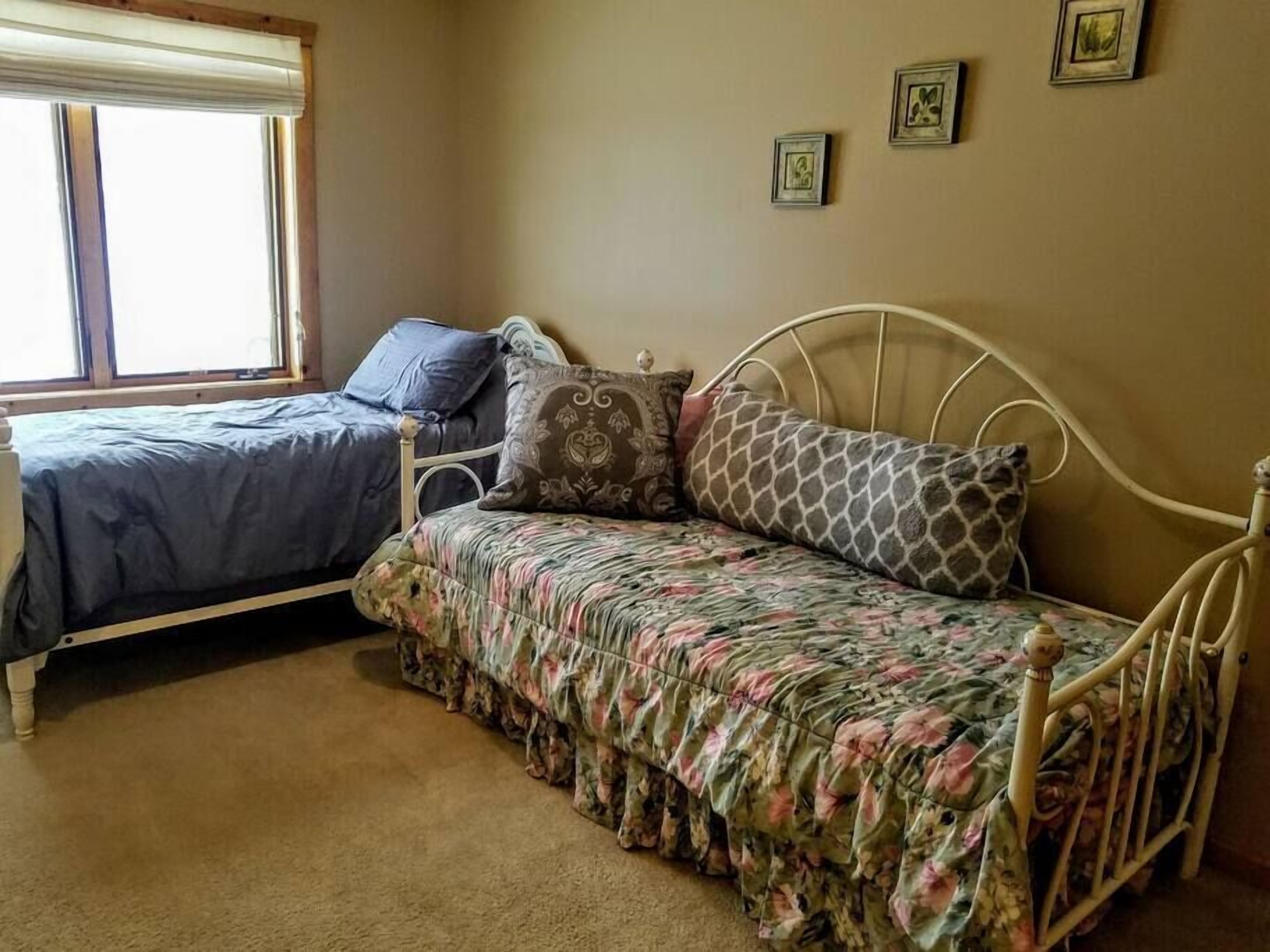 A bedroom with two beds, one with a blue bedspread and the other with a floral bedspread. There are three framed pictures on the wall.