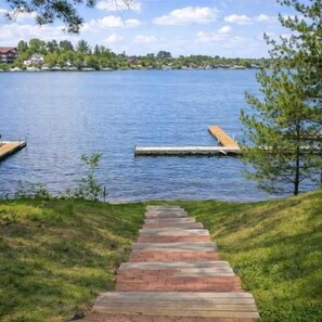 Un muelle de madera que se adentra en un lago, rodeado de orillas cubiertas de césped y árboles.