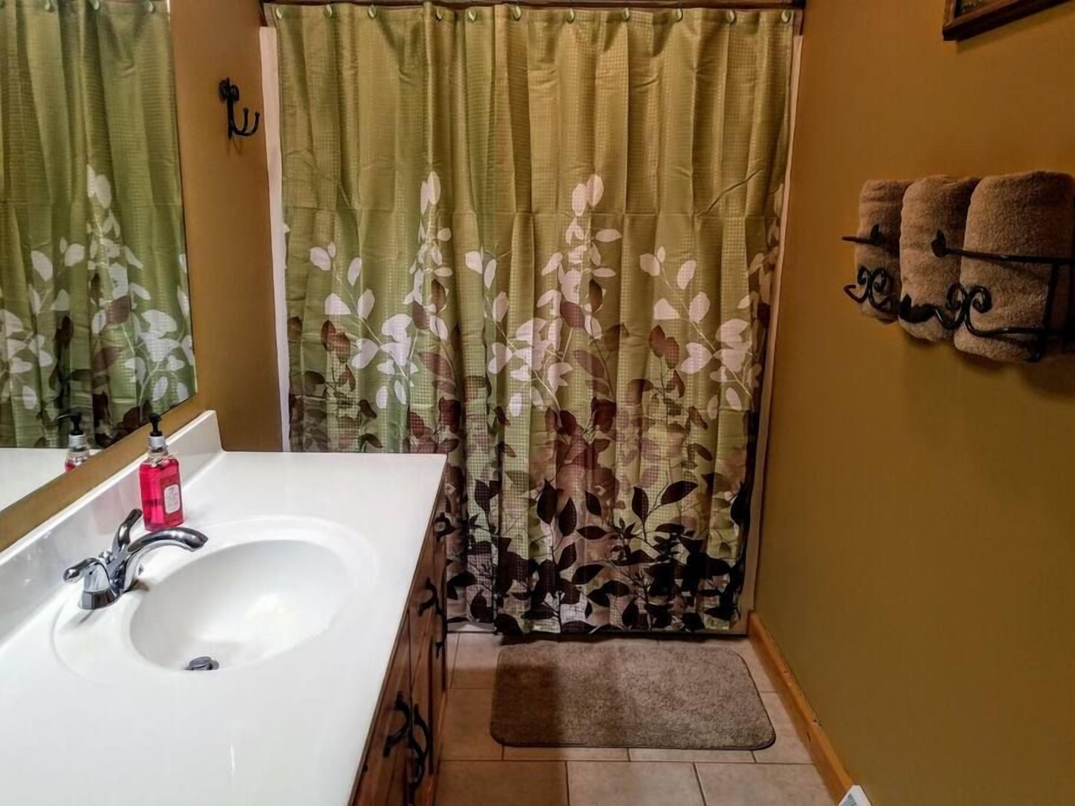 A bathroom with a white sink, a mirror, a floral shower curtain, and a towel rack with towels.
