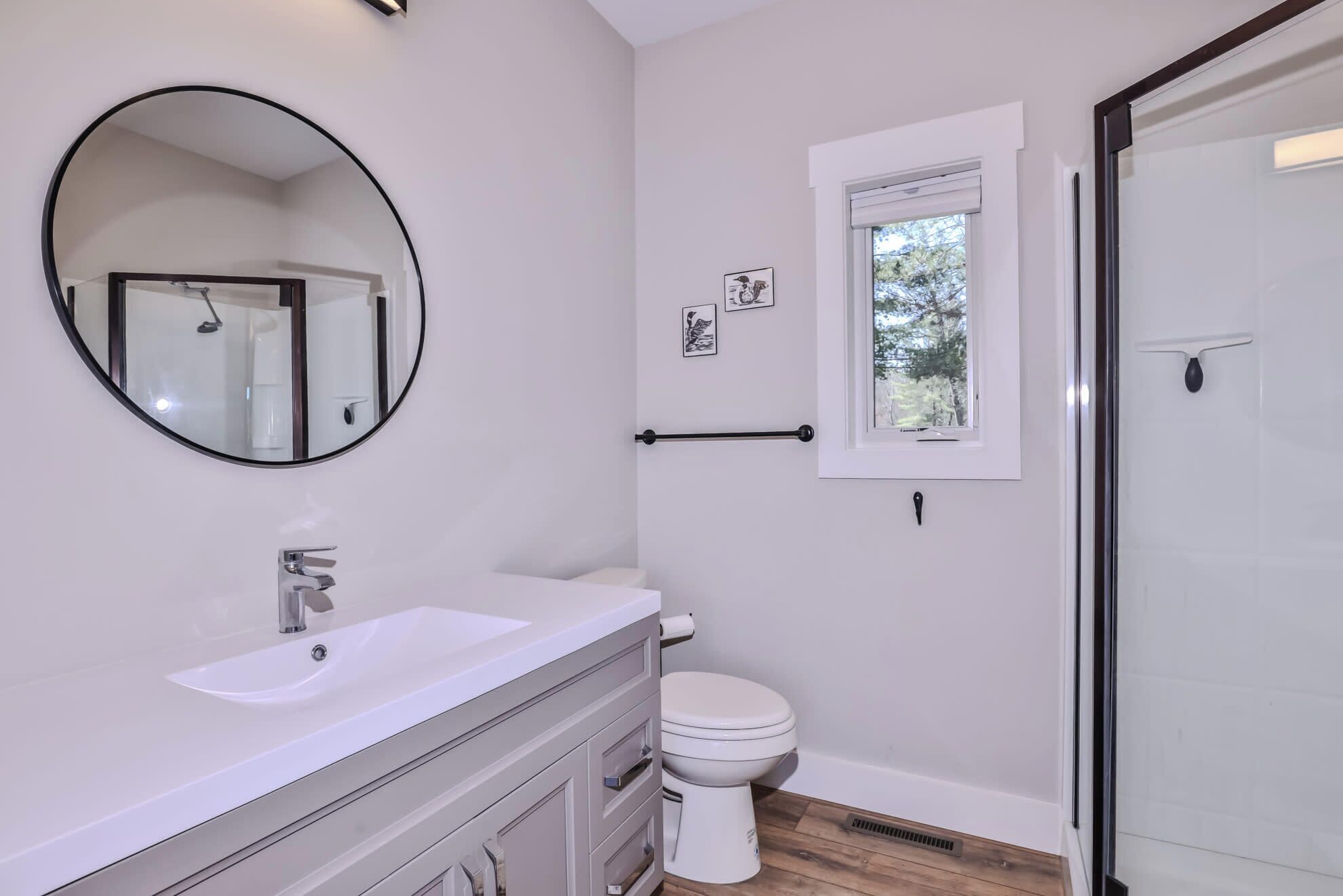 Une salle de bain moderne avec un grand miroir rond, un lavabo blanc, des toilettes et une douche à parois de verre.