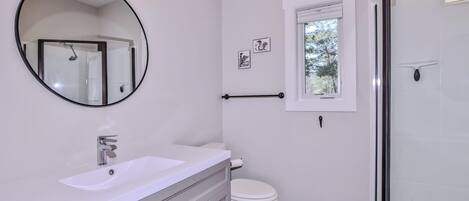 Une salle de bain moderne avec un grand miroir rond, un lavabo blanc, des toilettes et une douche à parois de verre.