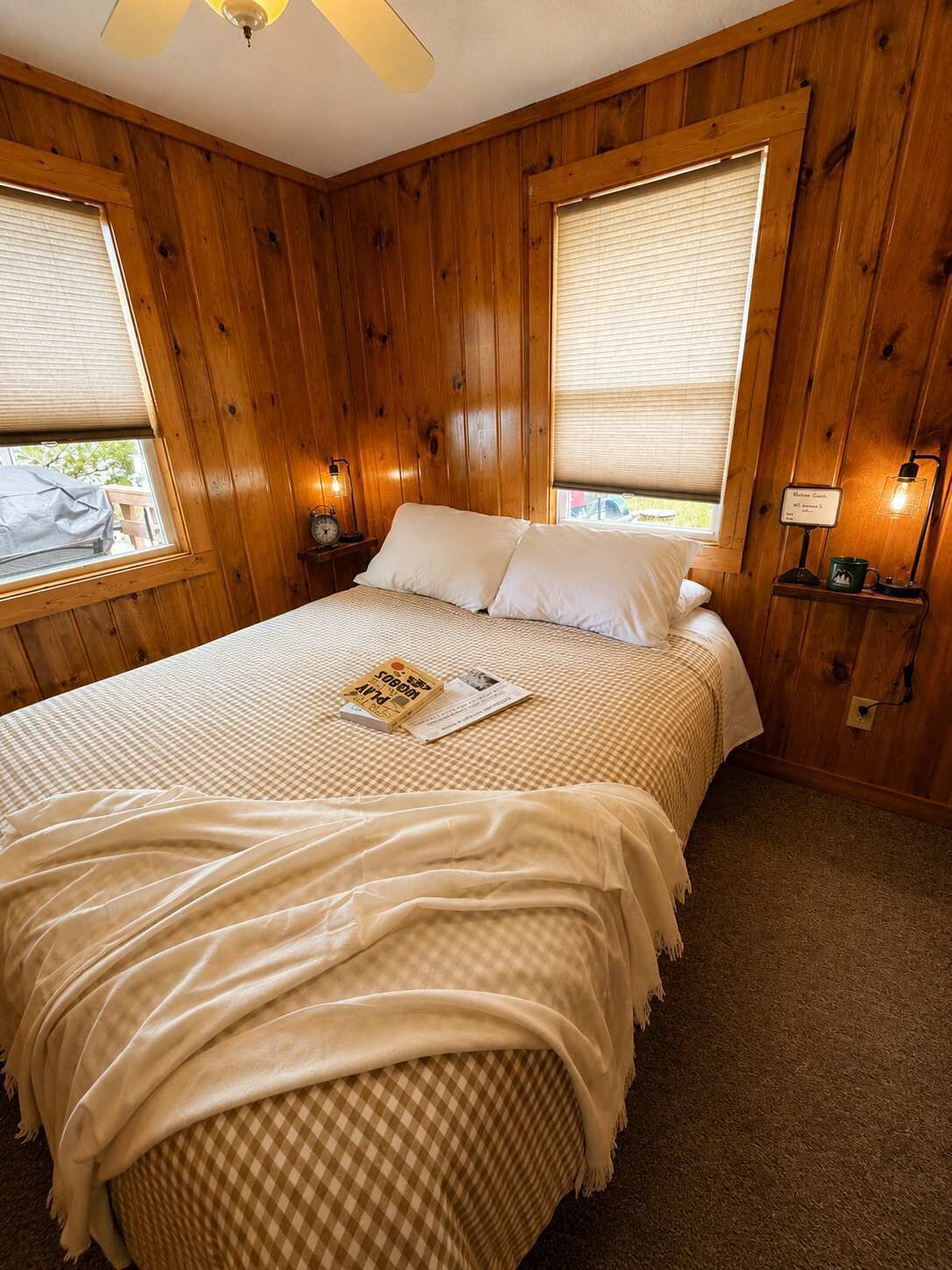 A wooden-paneled bedroom with a bed, two bedside lamps, and a window with blinds.