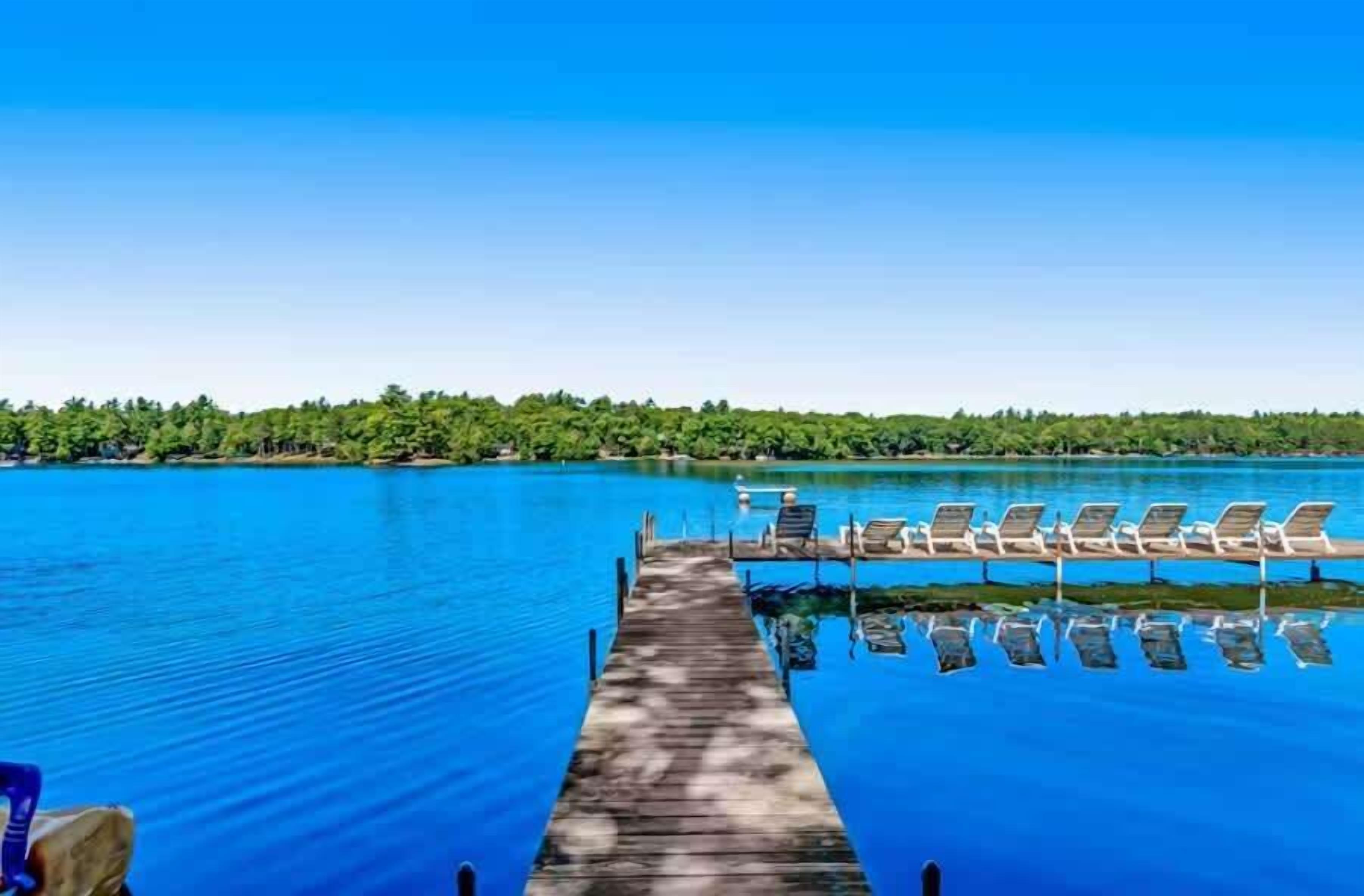 A wooden pier leading to a pool with lounge chairs.
