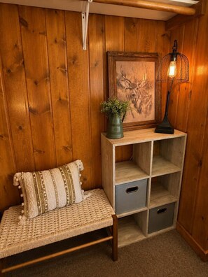 Een kamer met houten lambrisering, een bankje, een klein plankje met een plant, een lijstwerk met kunst en een tafellamp.