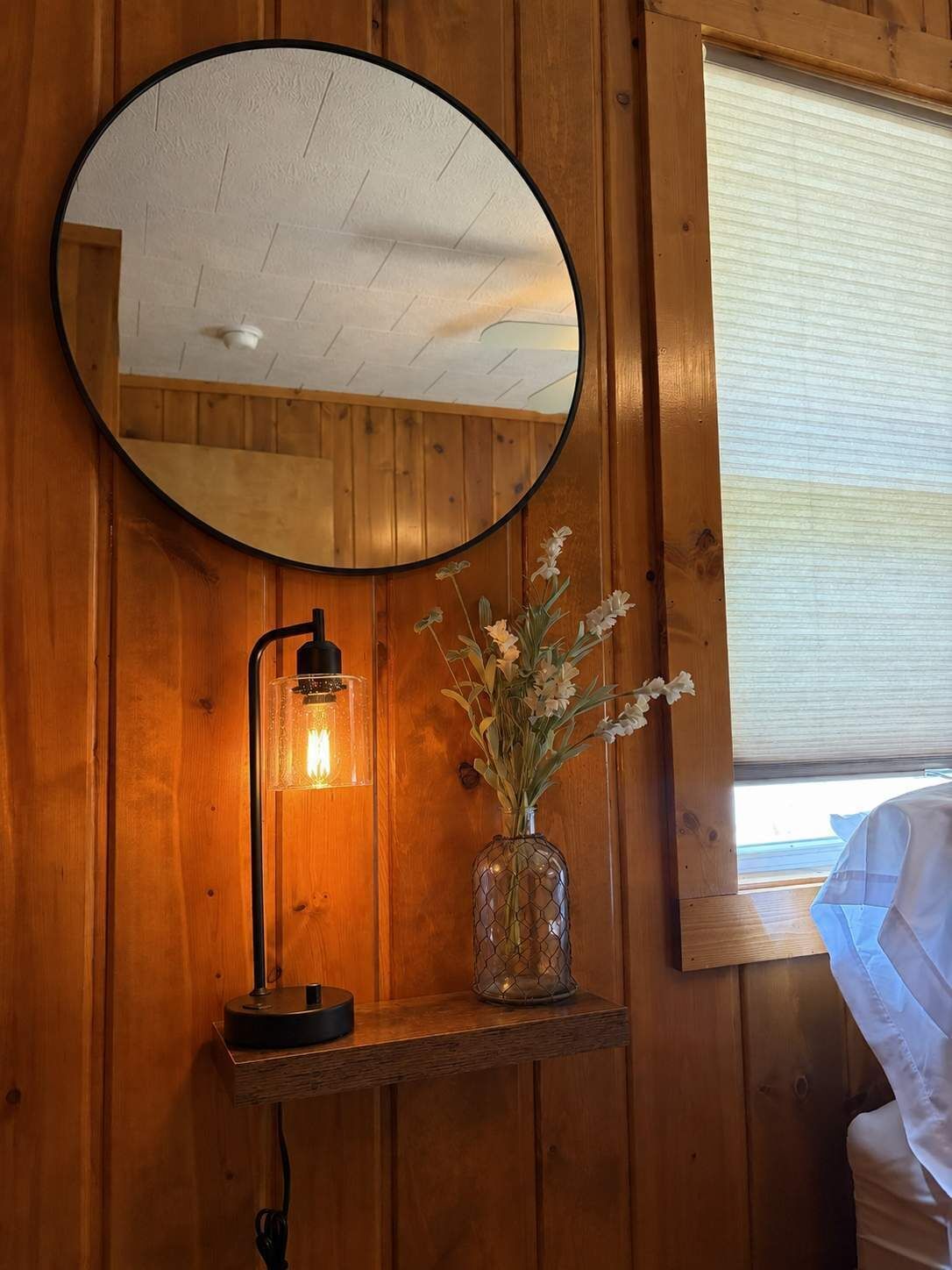 Un intérieur en bois agrémenté d’un miroir rond, d’une lampe de table et d’un vase rempli de fleurs.