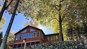 A wooden cabin with a stone wall in front, surrounded by trees. - Hilltop - Bouchard Shores Resort (Minocqua)
