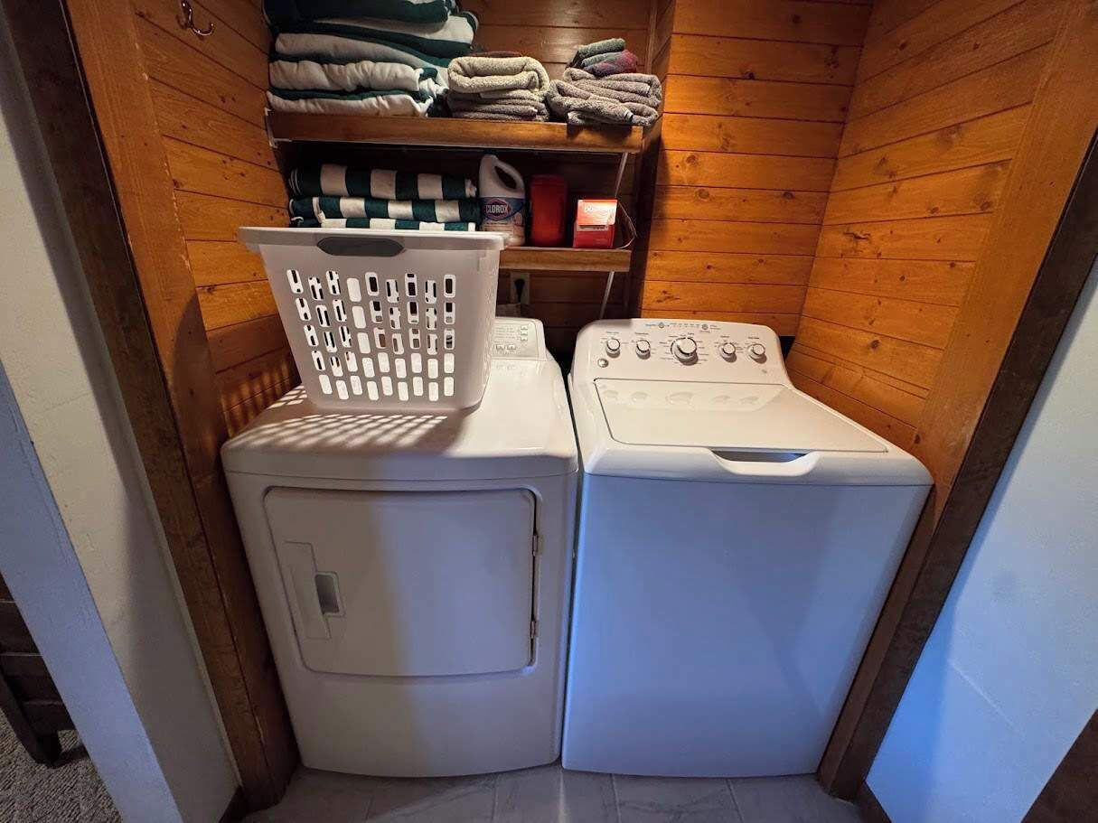 A laundry room with two white washing machines and a basket on the left.