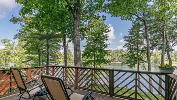 A wooden deck with two chairs and a railing overlooking a lake. - Hilltop - Bouchard Shores Resort (Minocqua)
