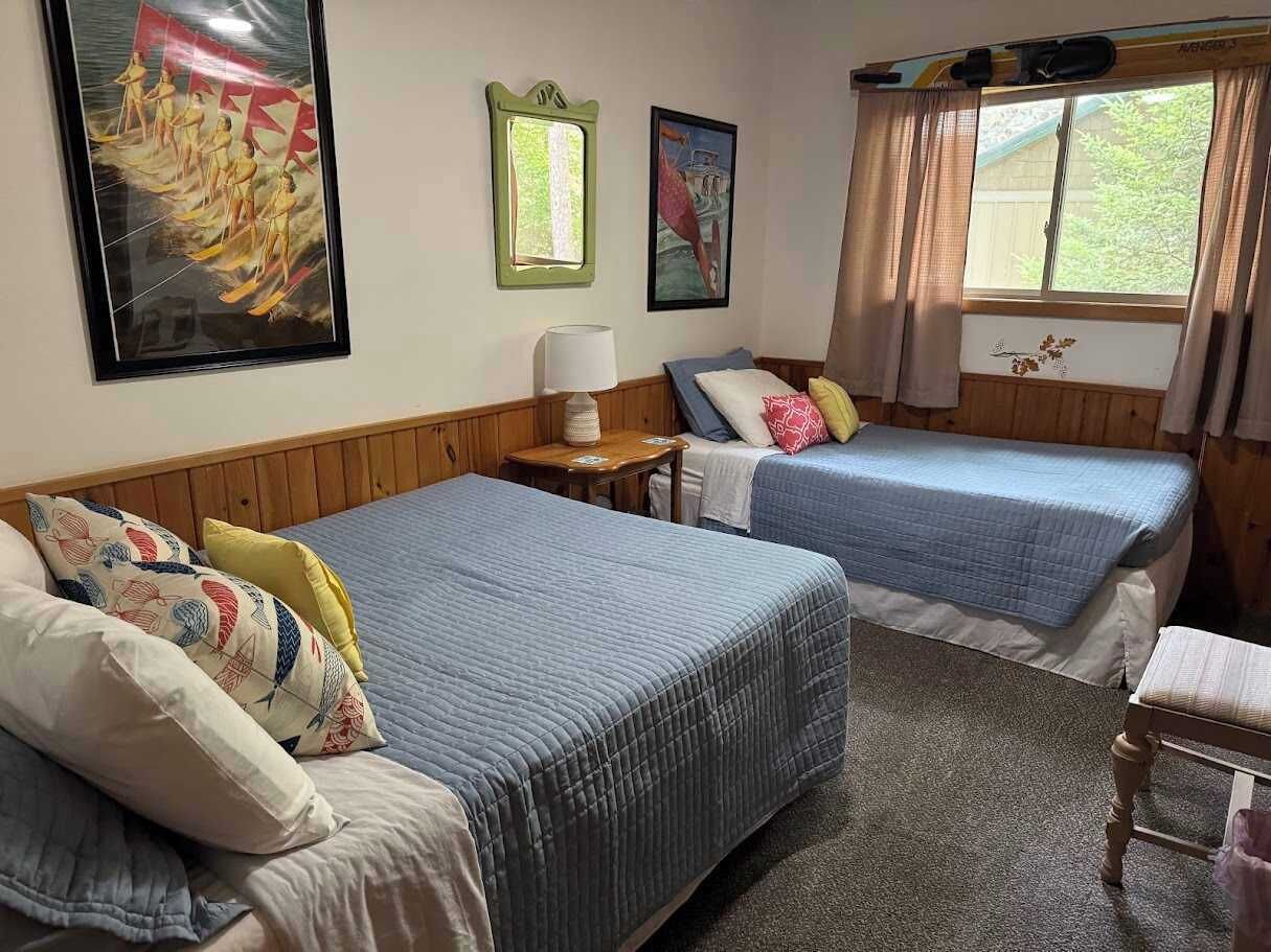 A room with two beds, a small table, and a window with curtains.