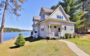A two-story house with a front porch, a small deck, and a view of a lake. - Eikedahls' Shoreview Lake House (Minocqua)