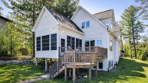 A two-story house with a deck, a covered outdoor area, and a stone wall. - Eikedahls' Shoreview Lake House (Minocqua)