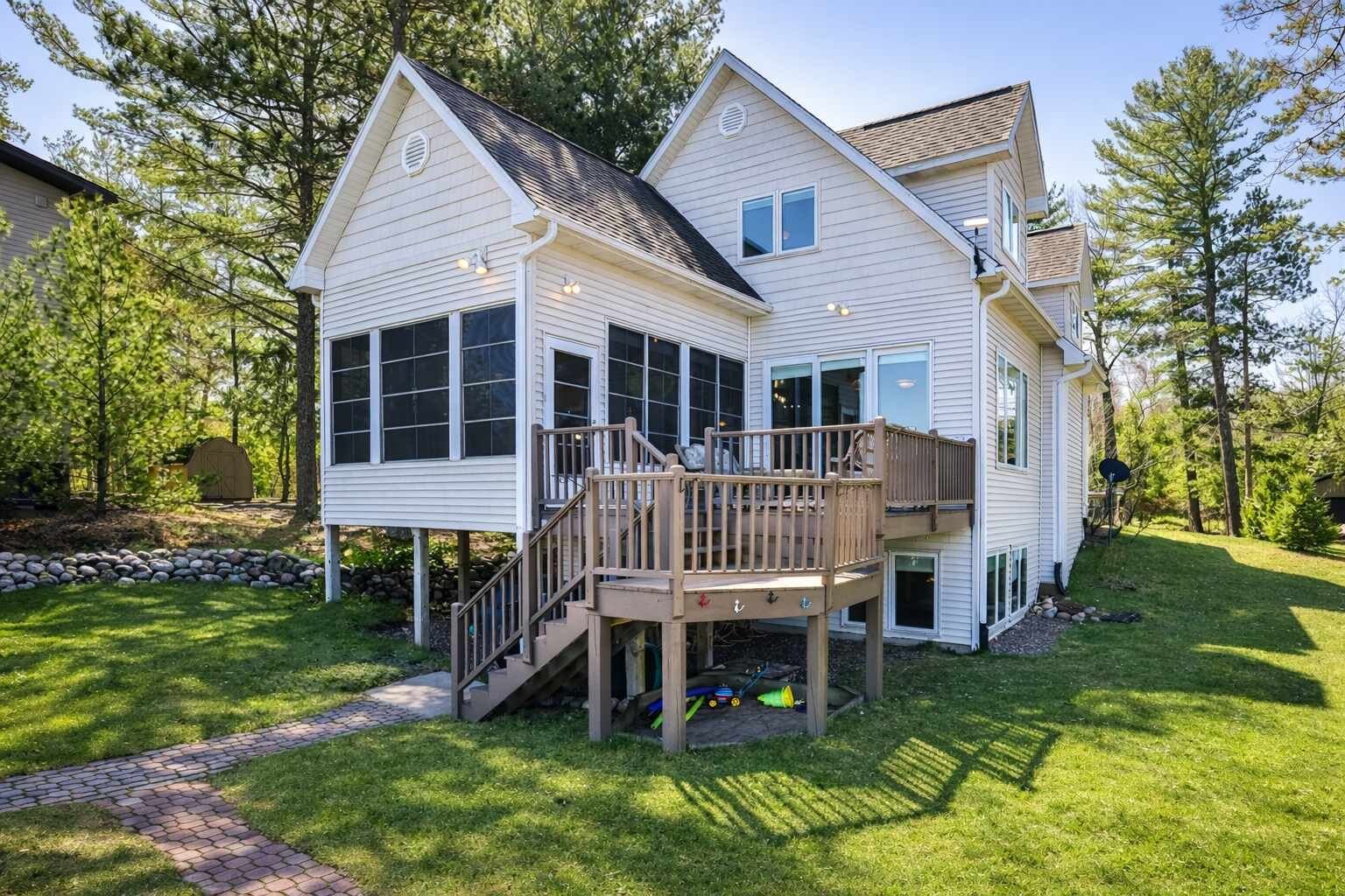 A two-story house with a deck, a covered outdoor area, and a stone wall.