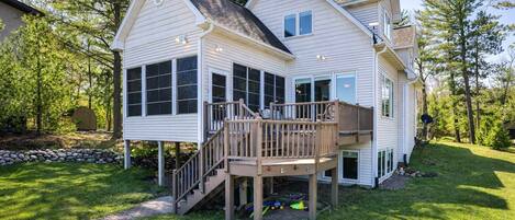 A two-story house with a deck, a covered outdoor area, and a stone wall.