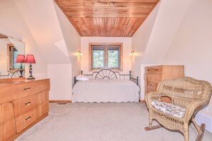 Camera da letto con un letto, una cassettiera in legno, una poltrona in vimini e una finestra con luce naturale.