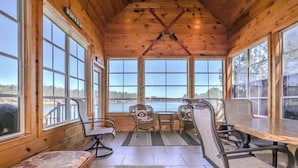 A wooden cabin with large windows, a wooden ceiling, and a view of a lake. There are four chairs and a bench. - Eikedahls' Shoreview Lake House (Minocqua)