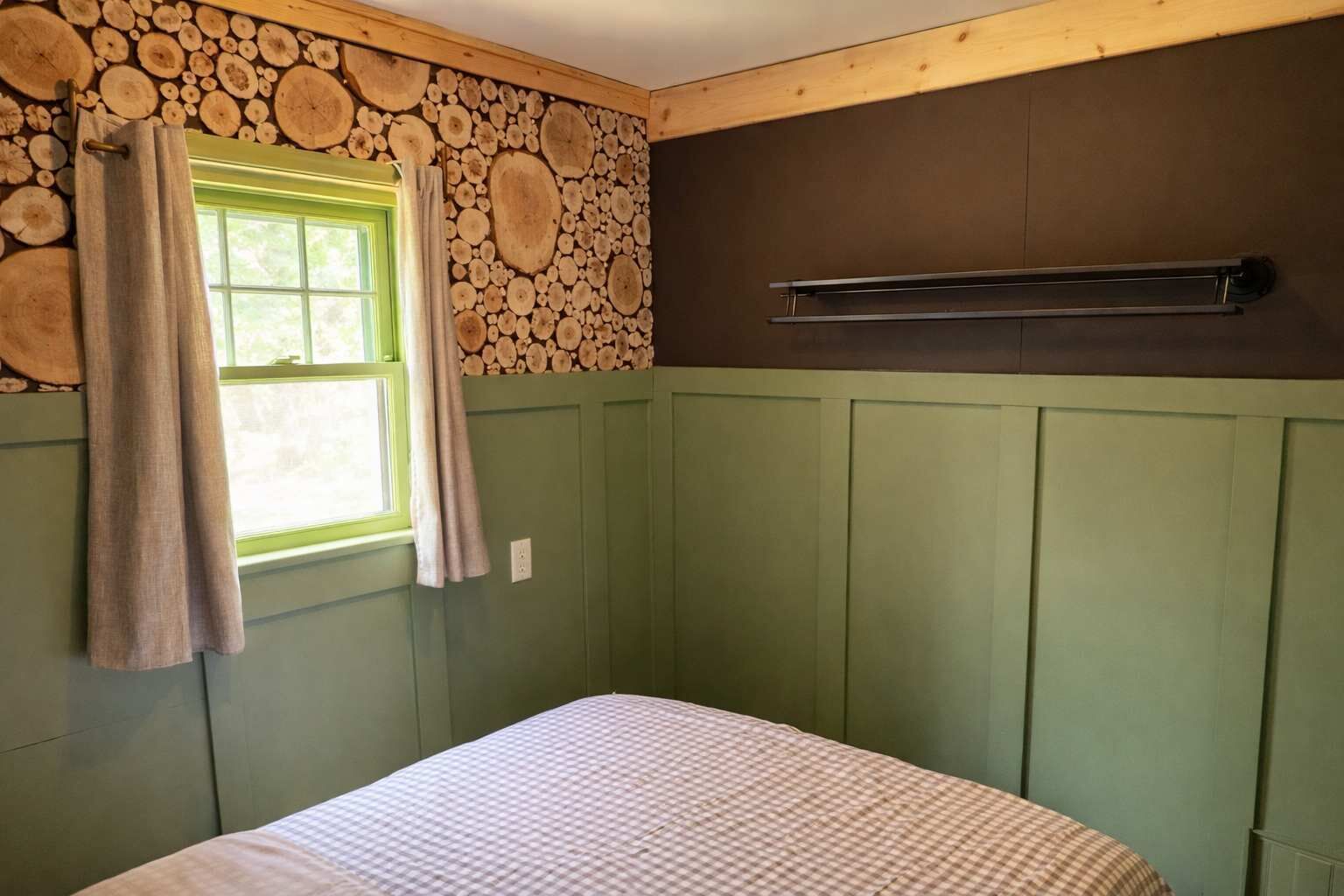 Une pièce avec un lit, une fenêtre avec des rideaux, un mur décoré d’un motif imitant des troncs d’arbres et un radiateur.