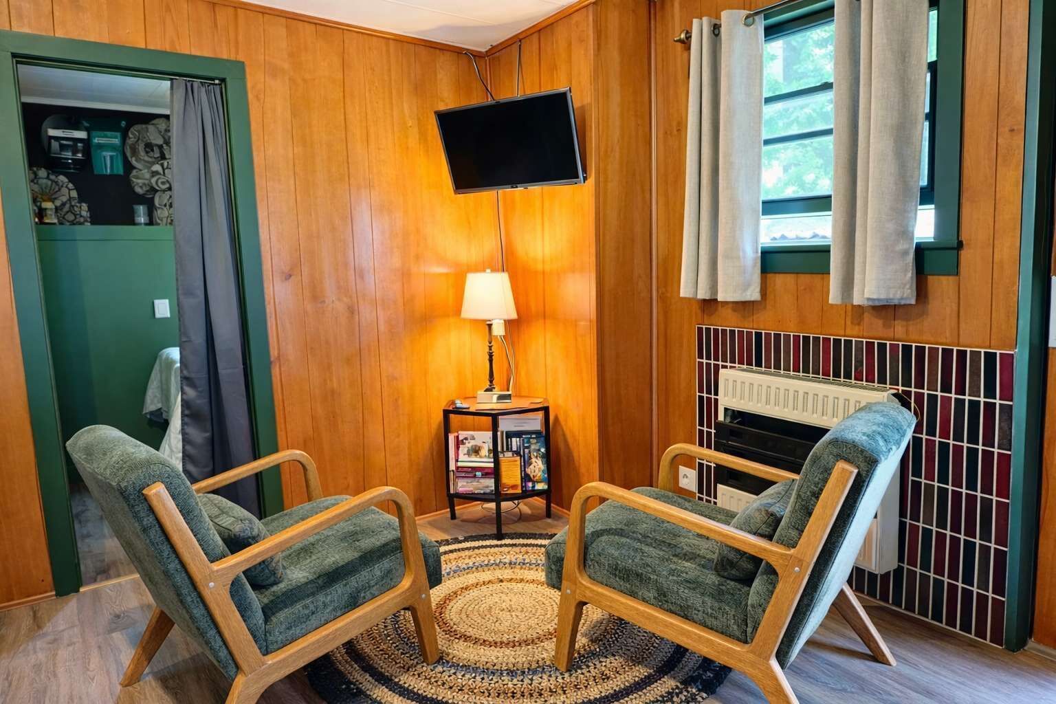 Une pièce chaleureuse avec des murs en bois, un téléviseur fixé au mur, une cheminée et deux fauteuils verts.