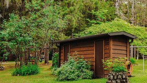 Une cabane en bois rustique, entourée d’une végétation luxuriante et d’un empilement de pierres.