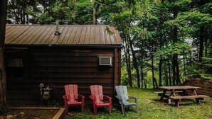 Une cabane rustique avec une façade en bois, un petit porche et deux chaises Adirondack.